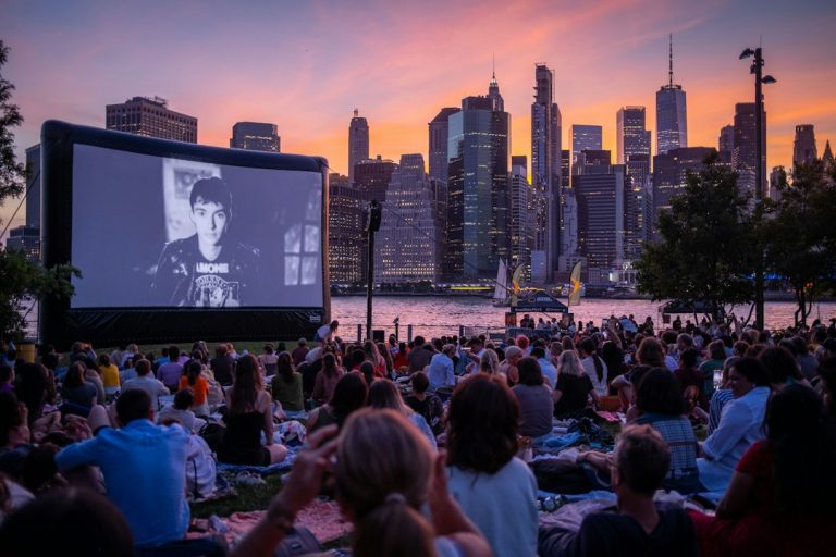 An outdoor movie audience at Brooklyn Bridge Park with a colorful sunset over Manhattan