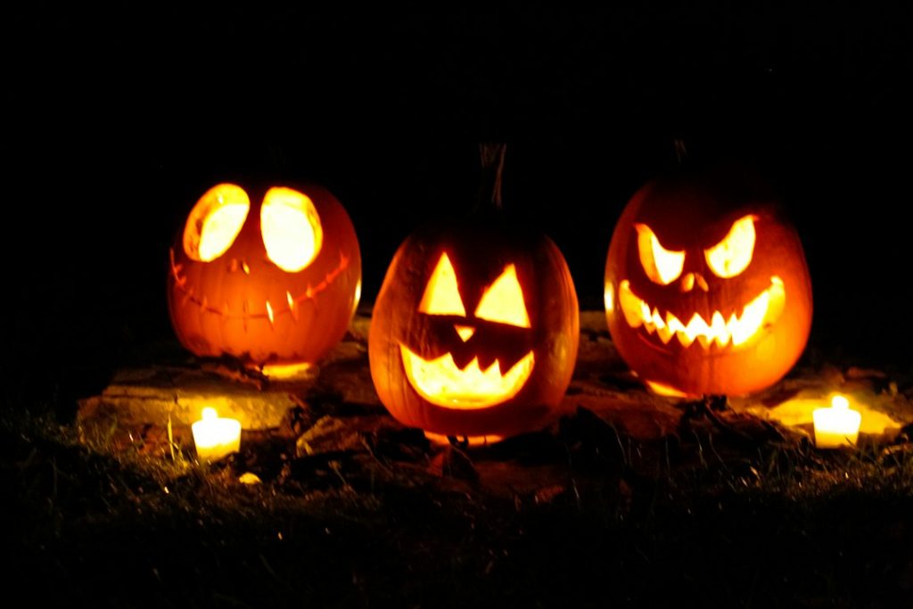 Three illuminated jack-o’-lanterns on fallen leaves at night; illustrative Halloween photograph