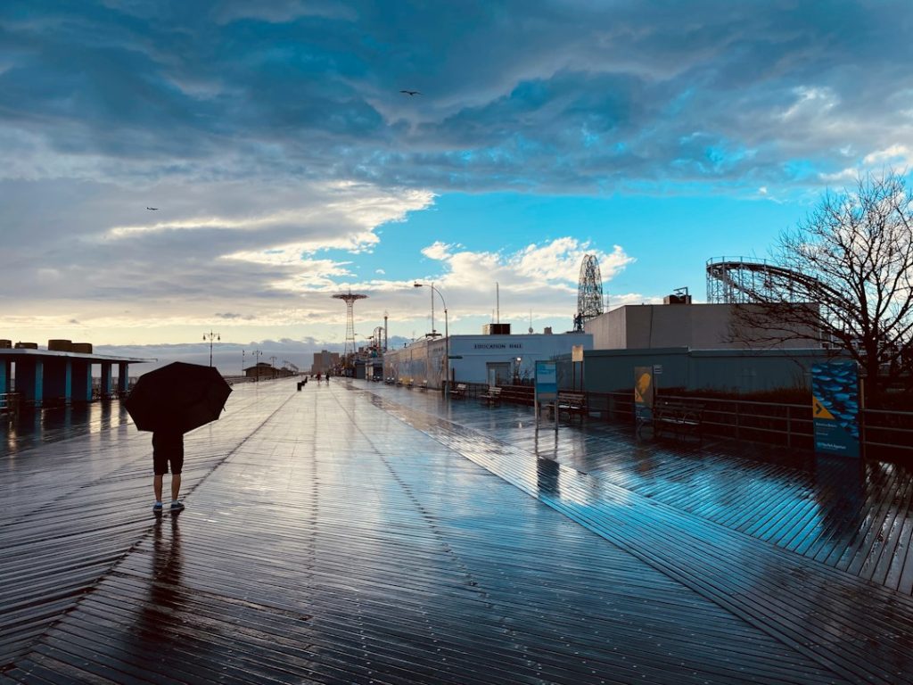 A person walking along a wet Coney Island boardwalk after a storm