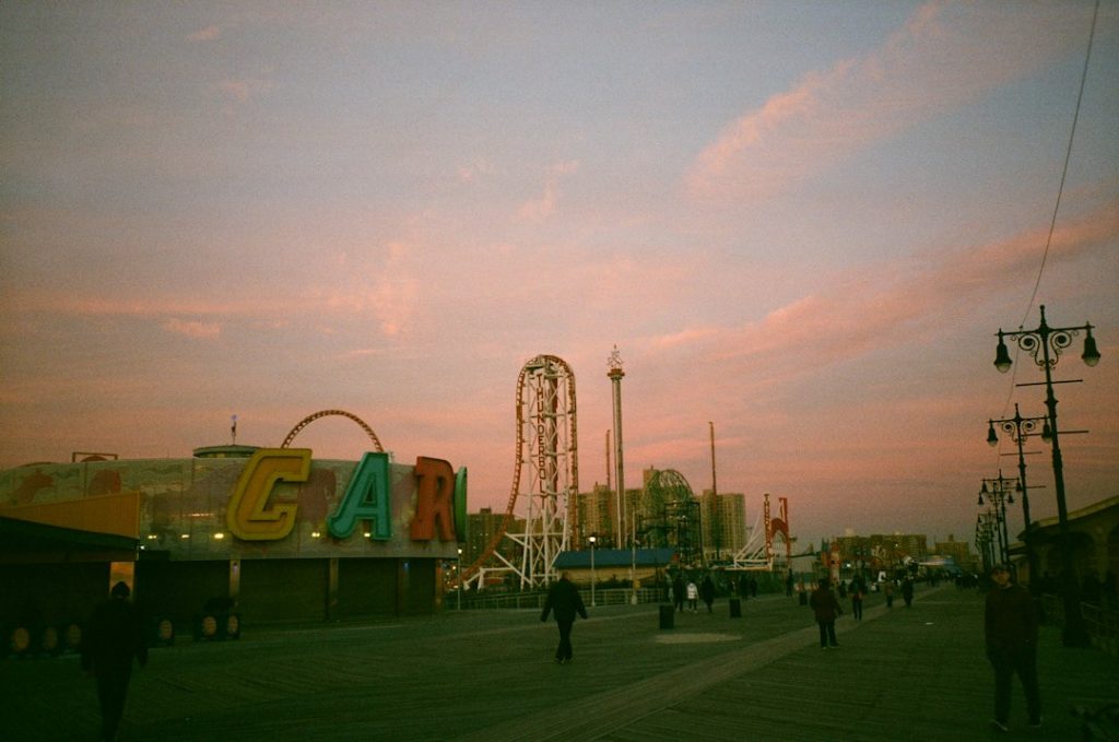 A Brooklyn seafront scene with amusement rides in evening light