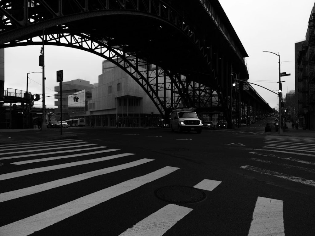 A black-and-white Harlem streetscape beneath an elevated structure