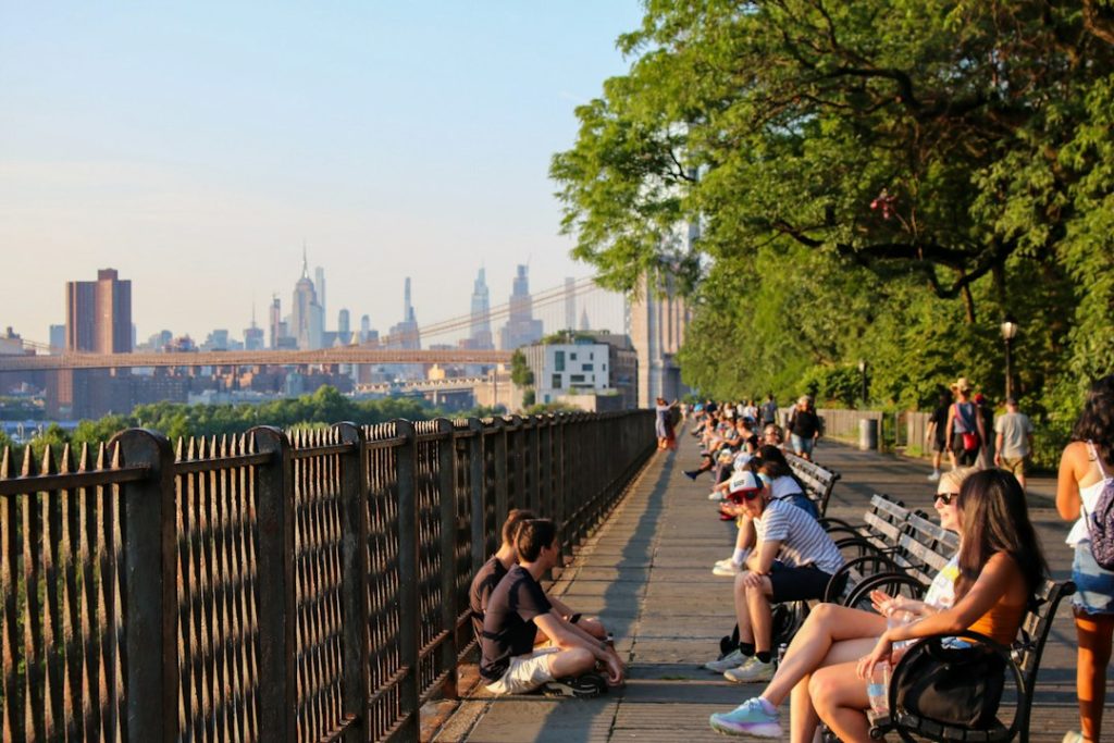 People relaxing on benches along a sunny Brooklyn waterfront walkway