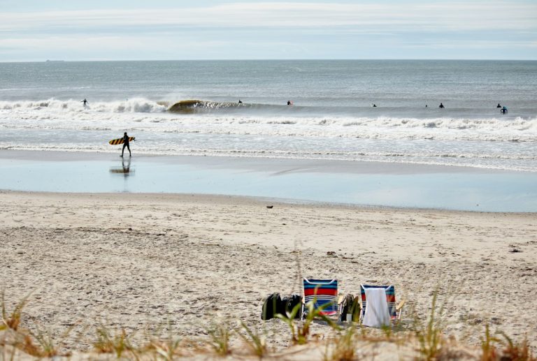 Beach chairs on the sand and surfers beside the waves at Rockaway Beach