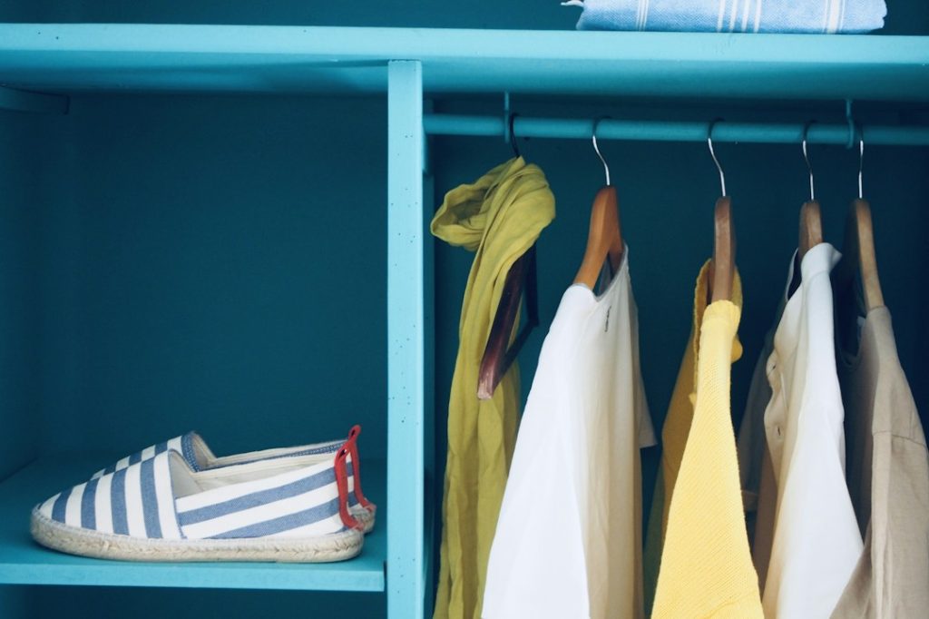 Neatly arranged clothes and striped shoes inside a blue closet