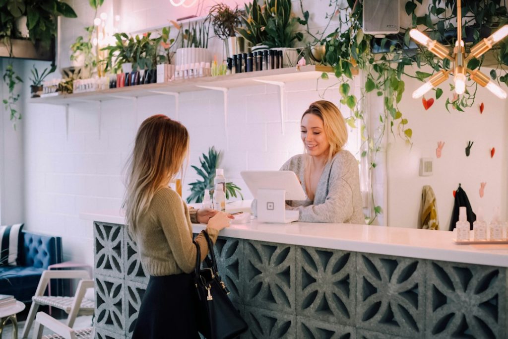 Smiling shopkeeper helping a customer at a bright counter surrounded by leafy plants