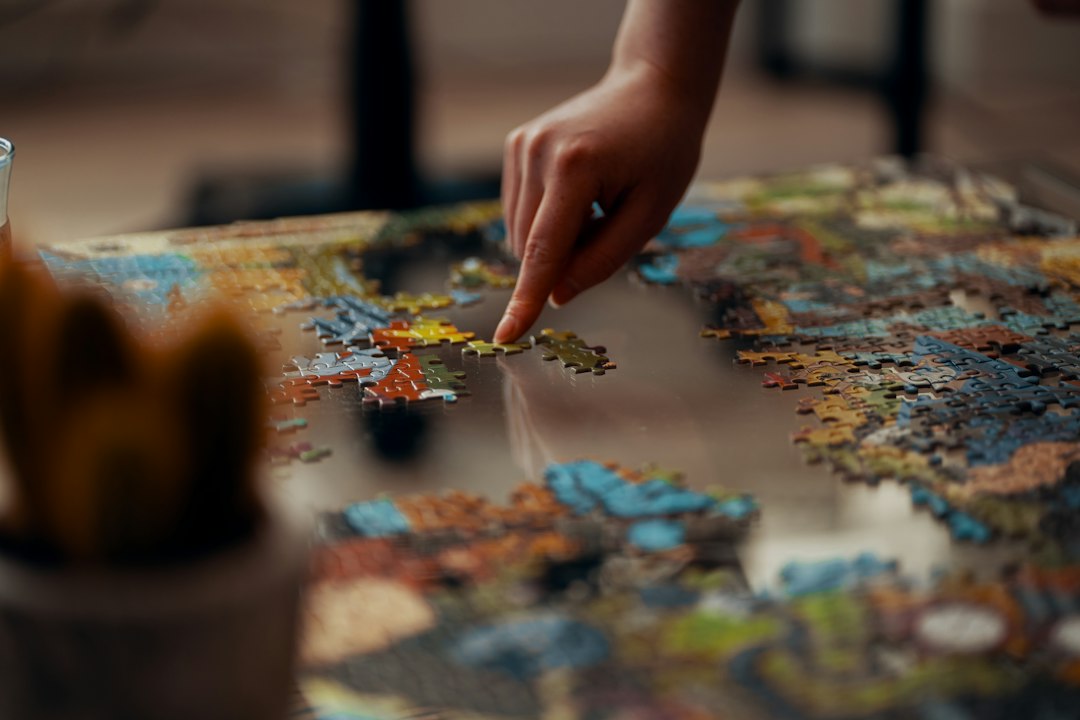 Hands assembling a jigsaw puzzle on a table; puzzle category inspiration