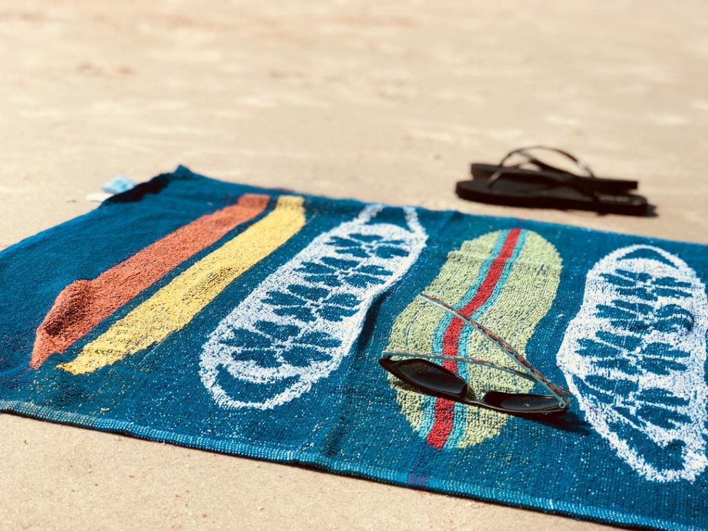 A colorful beach towel with sunglasses on the sand