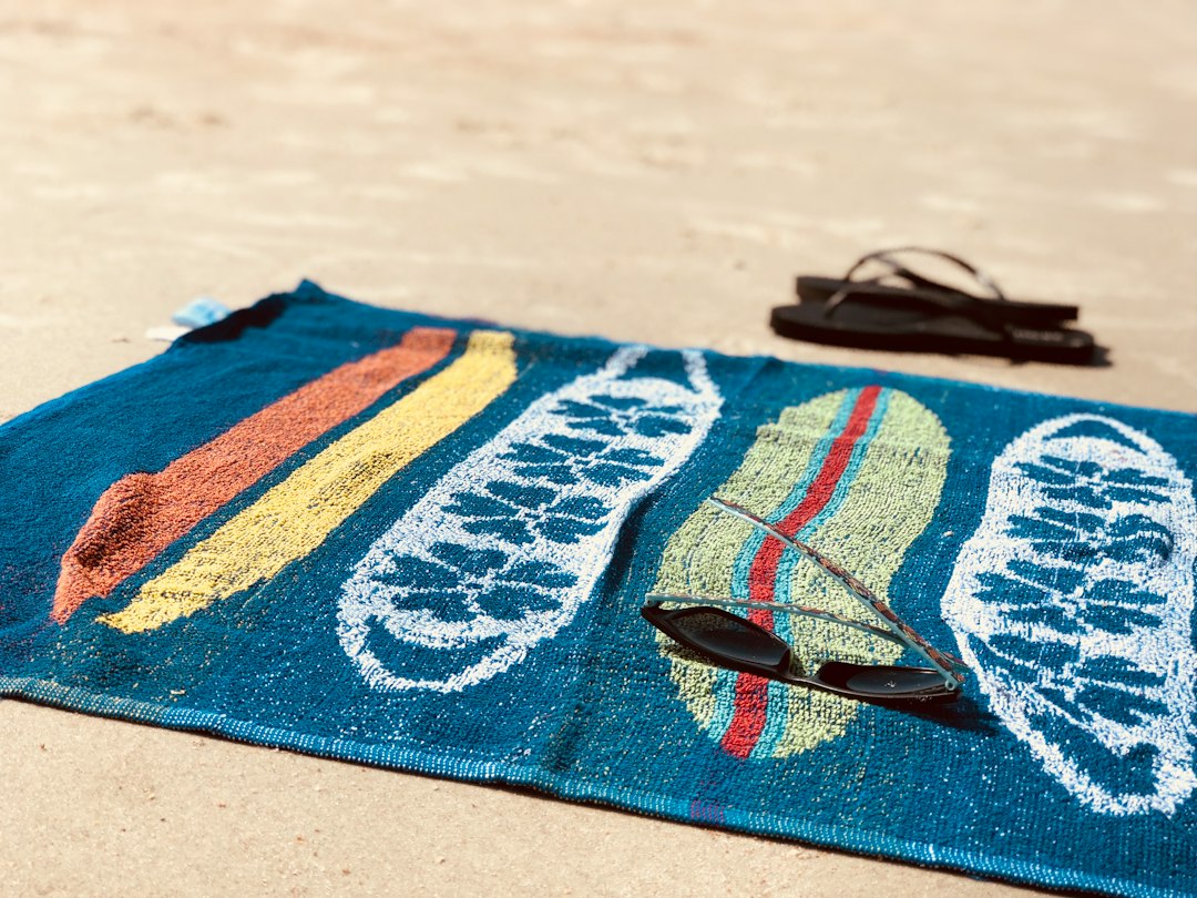 A colorful beach towel with sunglasses on the sand
