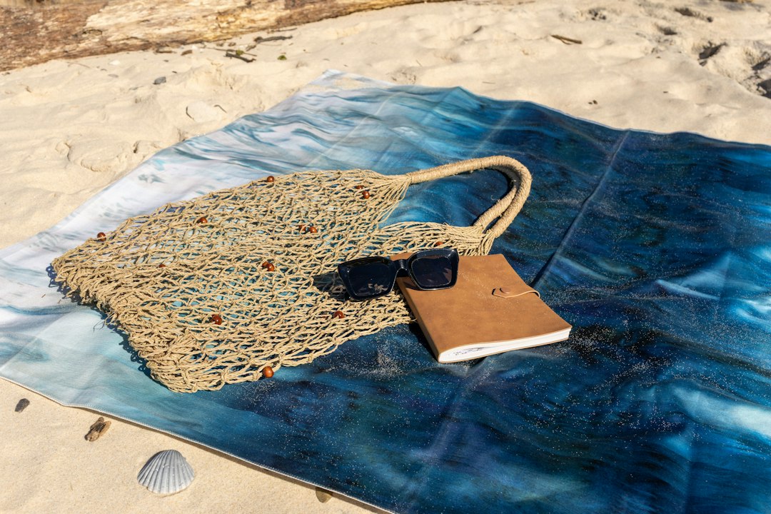 A beach tote, sunglasses, and notebook on a towel