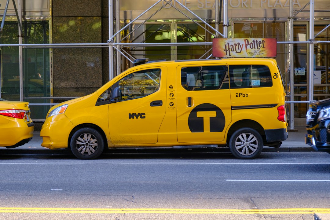 A yellow New York taxi passing a theatre poster