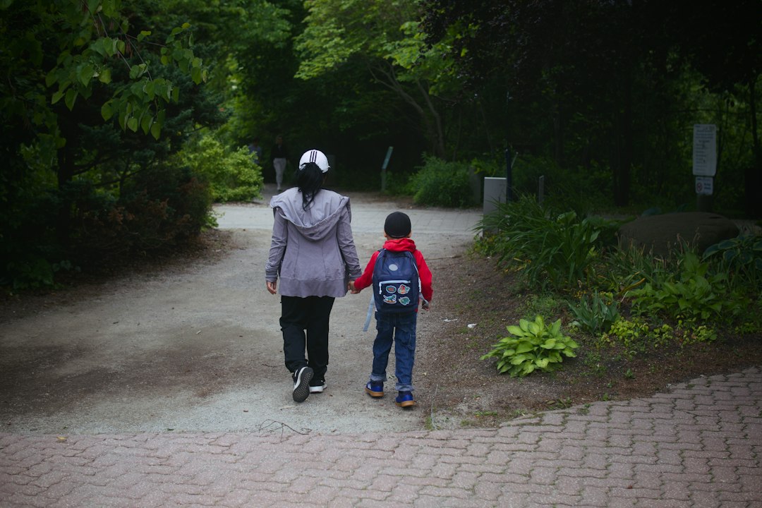 An adult and child walking together along a leafy park path
