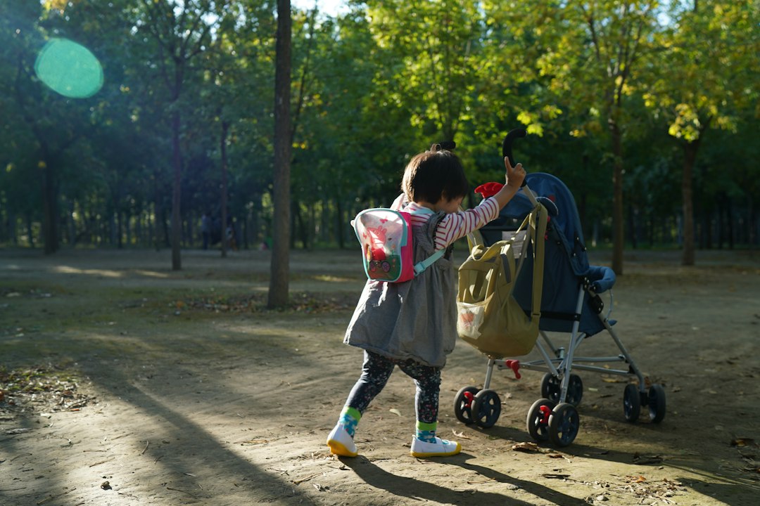 A child with a backpack beside a stroller on a sunny park path